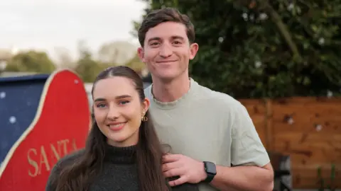 LondonIslandLiving Sacha and Matt stand in their garden in front of their sleigh boat smiling into the camera. Matt's hand is on Sacha's shoulder.