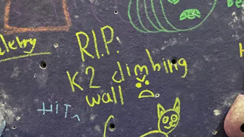 A message reading RIP K2 climbing wall is written in chalk