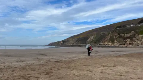 Saunton Sands beach with a kayaker walking on the beach carrying his kayak and paddle