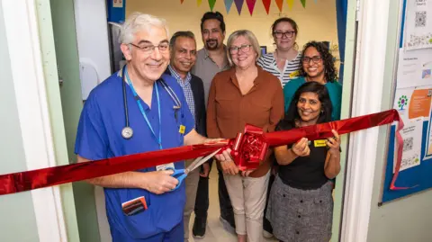 A groupl of people around a red ribbon which is being cut by the chief medical officer 