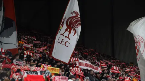 Reuters A wide angle of the crowd at Anfield Stadium. Liverpool fans are holding scarves and flags aloft as they sing.