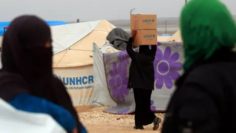 Getty Images A woman carries boxes of humanitarian aid supplied by Unicef at a refugee camp in Syria's north-eastern Hassakeh province on February 26, 2018