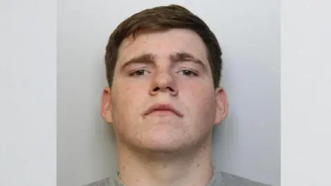 Custody image of James Doherty. He has brown hair and is wearing a grey top. He is looking directly into the camera.