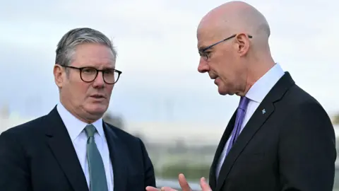 Getty Images Sir Keir Starmer, who has grey hair and is wearing dark glasses with a dark suit, white shirt and grey tie is talking with John Swinney. Mr Swinney is a bald man with glasses who is also wearing a dark suit and white shirt but with a purple tie