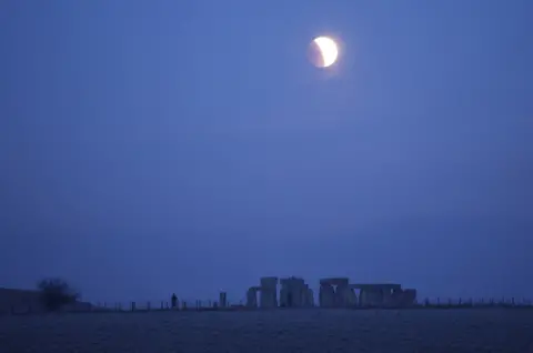 Reuters People view the full moon as a section moves into shadow during a lunar eclipse, before dawn, at Stonehenge stone circle, near Amesbury, UK