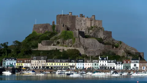 The image shows Gorey Pier, below Mont Orgueil Castle, on a sunny day. There is a clear blue sky.