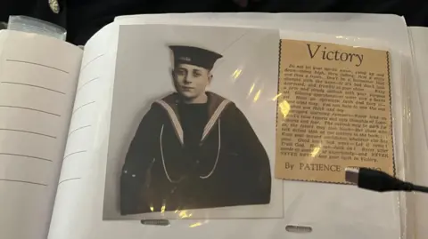 An old black and white photograph of Robin Boodle when he was a teenager in his Royal Navy uniform. The photograph is in a plastic sleeve and attached to a book which contains other photographs.