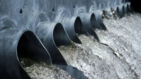 Getty Images Several dark coloured pipes are lined up beside each other with water running out. 