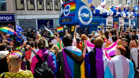 Getty Images A Brighton & Hove Albion FC bus passes revellers draped with Pride flags during the 30th anniversary Brighton & Hove Pride LGBTQ+ Community Parade on 6th August 2022 in Brighton