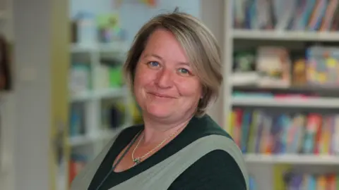 Joe Carnaby Leanne Fridd, who has brown, shoulder-length hair, smiles as she stands in her bookshop