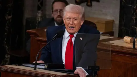 US President Donald Trump delivers his State of the Union address to a joint session of Congress in Washington, DC on February 24, 2026. The president is wearing a dark blue suit and a red tie. 