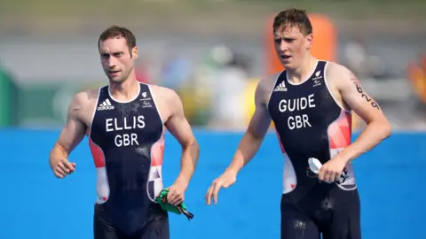 Dave Ellis and Luke Pollard both in Team GBR swimsuits holding swimming hats and goggles in one hand