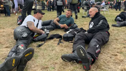 Three men in biker gear lie down on the grass at the event on Sunday