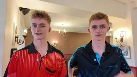 Twins Harry and Alfie at the darts academy in Newton Abbot. Alfie is wearing a red top and Harry is wearing a navy blue top. 