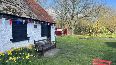 Helen Mulroy/BBC A building, daffodils and bunting in Thriplow, Cambridgeshire