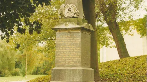 Chris Smith/West Yorkshire Fire and Rescue A stone memorial with gold lettering in a green wooded area of a cemetery.