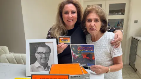 Julia Gregory/BBC Ms Camby and her mum Norma, with Dungeons and Dragons memorabilia and a photo of Mr Douglas