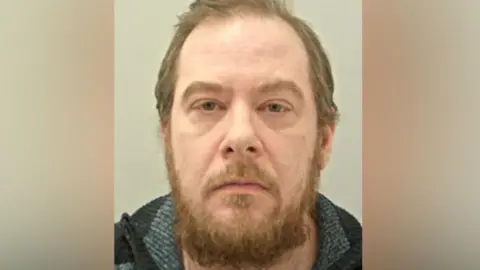 Police custody image Chris Wearing with brown hair beard wearing a grey and black knitted jumper