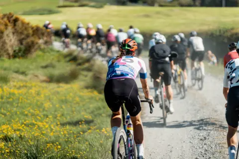 Red On Sports Cyclists pedal off into the distance along a dusty track