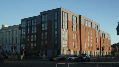 Parliament Place in Liverpool. It is a five story block clad in brick and grey composite, at the corner of a busy main road. 