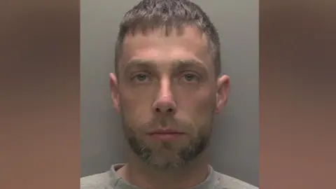 Humberside Police Custody mug shot of Battams who has blue eyes, mousey brown stubble and cropped hair and is looking solemn. He is wearing a grey sweatshirt