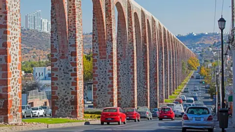 Arterra/Getty Images The stone arches of Querétaro's aqueduct run into the distance next to a road