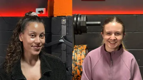 Rhianna Venables/BBC The head and shoulders of Kathryn, with curly brown hair smiling at the camera. She is wearing a black fluffy zip-up jacket. On the right, Beth has straight blonde hair and is smiling at the camera. She is wearing a pink zip-up sweatshirt.