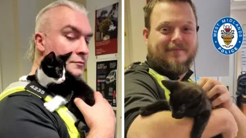 West Midlands Police Two police officers in uniform can be seen posing, each with a kitten. One of the kittens is black with white socks and chest, while the other is all black.