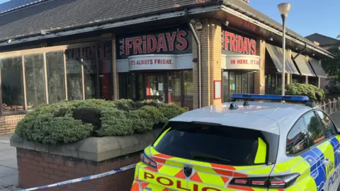 Oli Constable/BBC A police car outside a closed TGI Fridays restaurant. Police tape has sealed the location off. 