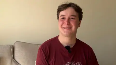 Nineteen-year-old Dmytro. He is wearing a red t-shirt and is sitting on a sofa.