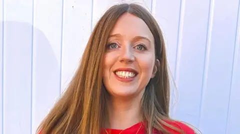 Wessex Health Partners Dr Elizabeth Jones, a woman with long hair and wearing a red top, is pictured smiling at the camera. 