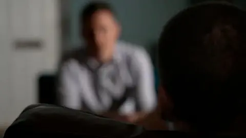 Blackout of interviewee with fuzzy shot of BBC journalist in the background.