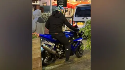 A man on a motorcycle. He is wearing black clothes and the bike is blue. 