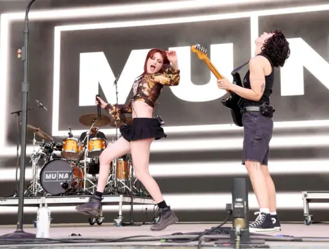 Getty Images Muna on stage at the Bonnaroo music festival in 2023. Katie is leaping into the air, while Josette throws her head backwards, mid-guitar solo.