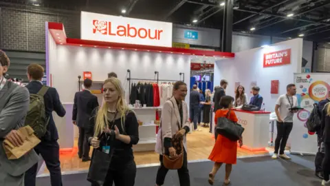 Women at Labour conference in front of a stand selling merchandise branded with the Labour party logo