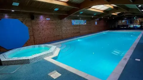 An empty indoor swimming pool, with a smaller octagonal pool located at one of the corners.