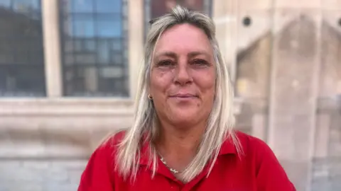 A woman in a red top looks at the camera