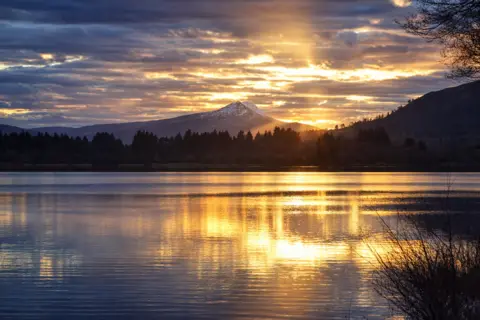 John Connelly A snow-capped Ben Lomond in the distance, with Lake Menteith in the foreground, the sun is reflected on the rippled water.