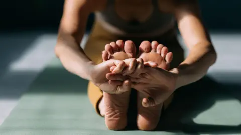 Getty Images A stock picture of a woman - just her feet and body fully in picture - stretching her legs while doing yoga