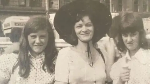 JACKIE HALLAM A black and white holiday photo of Jane, Lorna and Jackie smiling. Jackie is holding an ice cream. 