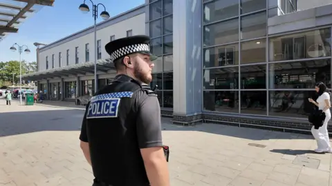 PC Tom Byrne in his police uniform walking on the streets of Shirley looking around by a supermarket.