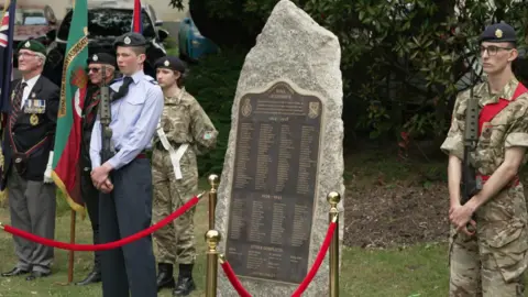 the large granite stone showing a plaque featuring names.