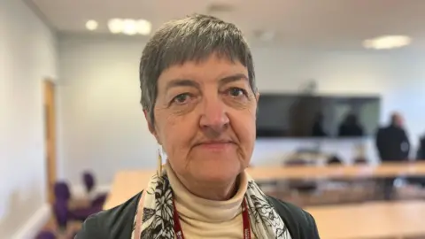 Una mujer con cabello corto y gris mira a la cámara.