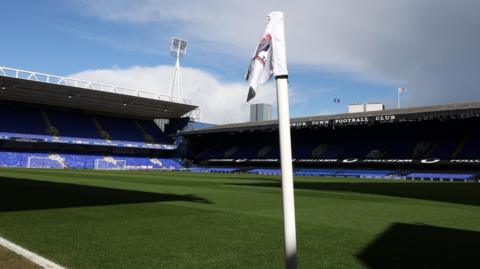 A picture of an empty Portman Road from the corner flag. The flag is in the foreground in the middle of the picture with two stands shown, one behind the goal and the other on the far side of the image.