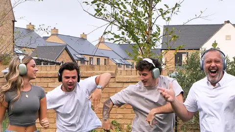 The Famileigh Darcy, Harrison, Travis and Paul all dancing in their garden, with headsets on. Paul is looking at the camera and smiling, Darcy is looking at Harrison and Travis to the ground.