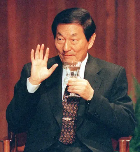 Boston Herald via Getty Images Then-Chinese Premier Zhu Rongji, wearing a suit and holding a glass, waving to well-wishers following a speech at the Massachusetts Institute of Technology in the US in 1999