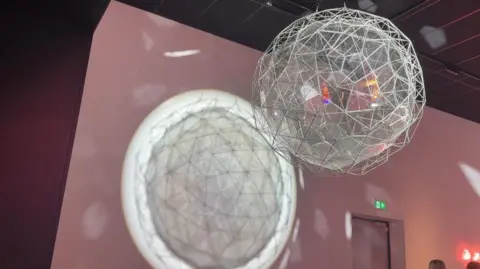 One of the features of the exhibition. A poloygonal sphere - if you can still call it a sphere- is suspended from the ceiling. It seems to be made from some kind of wire and glass combination. A light is being shone through it, which creates a geometric pattern on the wall of the darkened room.