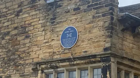 Grace Wood/BBC A circular blue plaque above a window on an old stone building. It reads: The Paper Hall