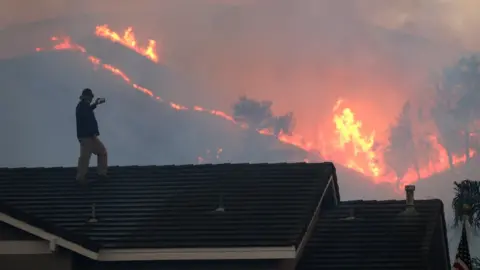 Getty Images CHINO HILLS, CA - OCTOBER 27: Herman Termeer (cq) watches the brushfire at Chino Hills State Park from the roof of his house on Tuesday, Oct. 27, 2020 in Chino Hills, CA. (Photo by Myung J. Chun/Los Angeles Times via Getty Images)