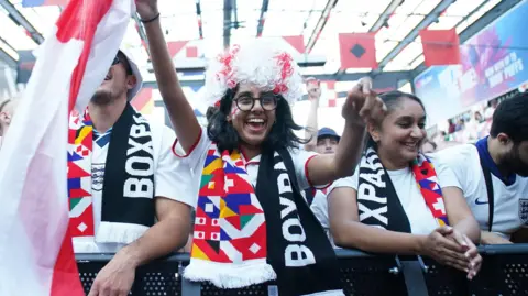 Una mujer ondea la bandera de Inglaterra frente a una multitud de aficionados.